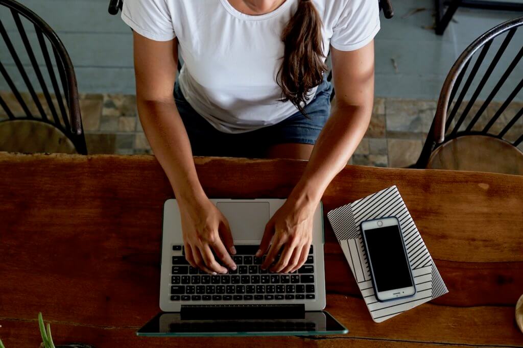 best blogging courses explained, overhead view of a woman sitting at a laptop wearing a white shirt