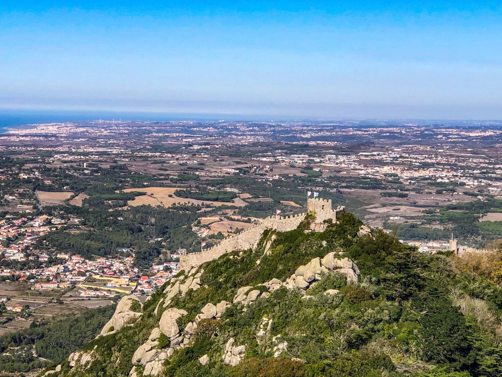 A panoramic view of the Moorish Castle in Sintra with the countryside in the background and ocean in the distance