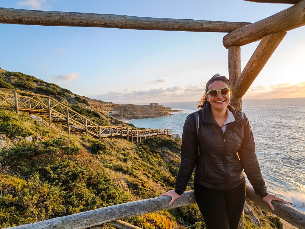 Nicola smiles while standing on a wooden staircase overlooking Ribeira D'Ilhas beach