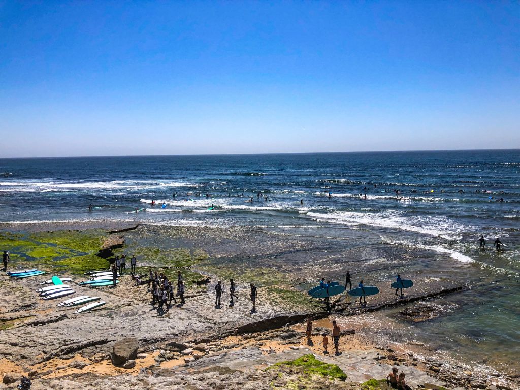 Taking a surfing lesson is one of the best things to do in Ericeira Portugal. In this image, groups of surf schools are walking out into the ocean at Praia do Matadouro