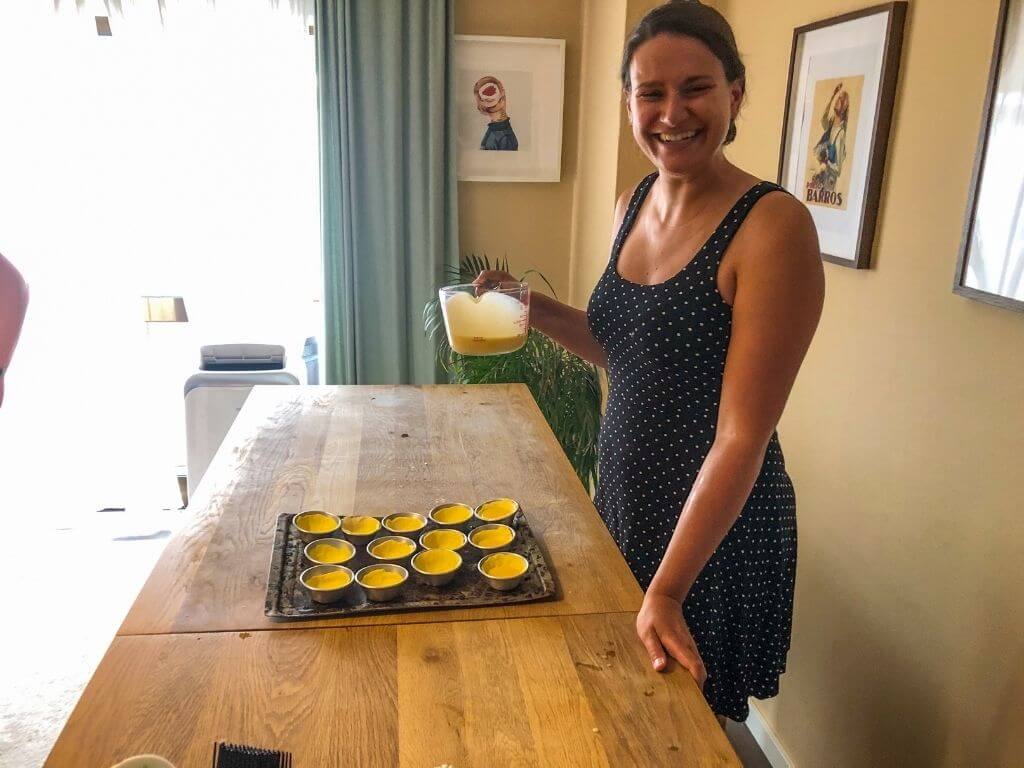 Nicola holds a measuring cup filled with pastel de nata filling over a tray of crusts in little tins