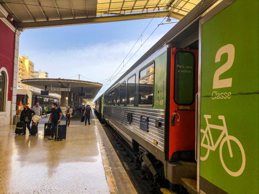 People with luggage walking next to a modern train at the Porto train station.