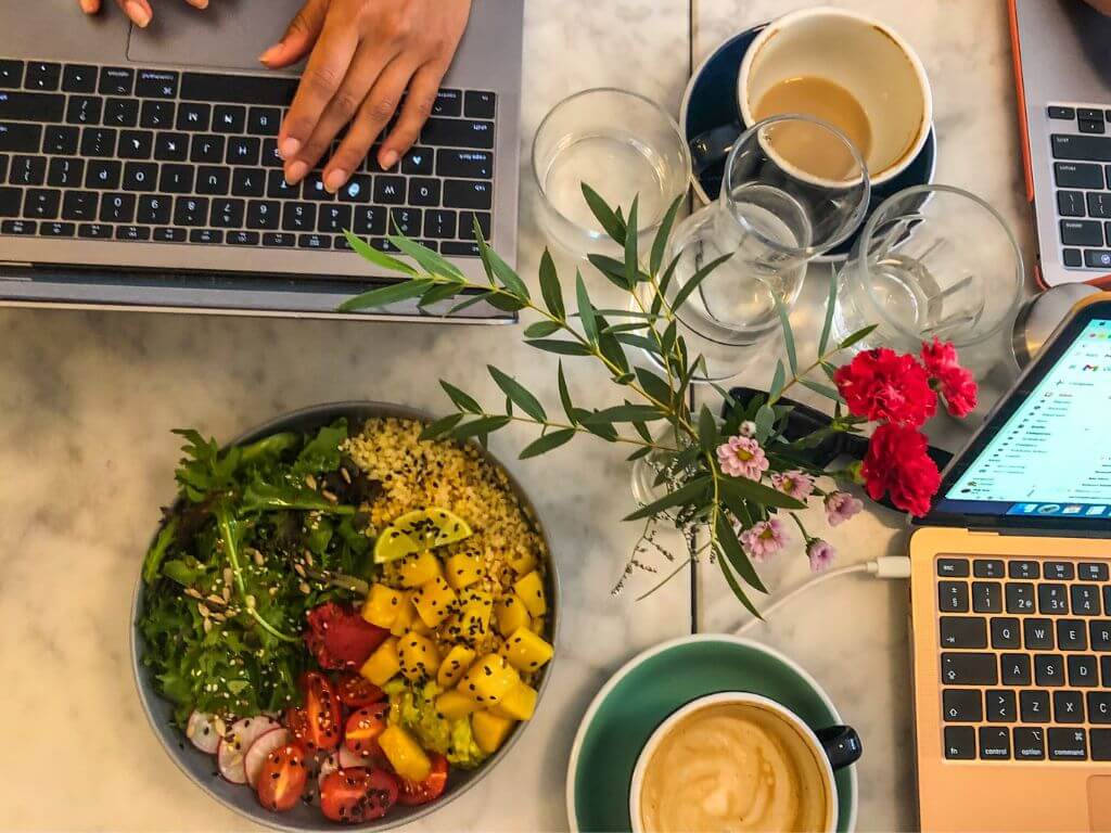 A table with a breakfast bowl and coffee cup with two people working at laptops at Bowls and Bar Lisbon
