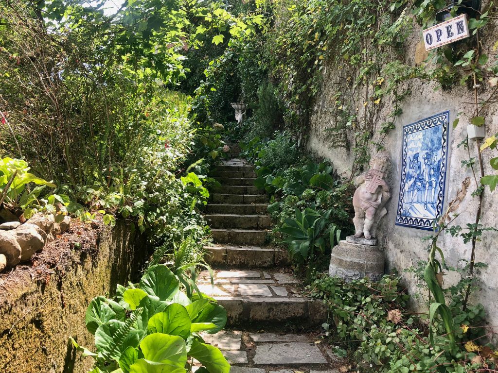 A path surrounded by gardens with a blue tile sign that says welcome