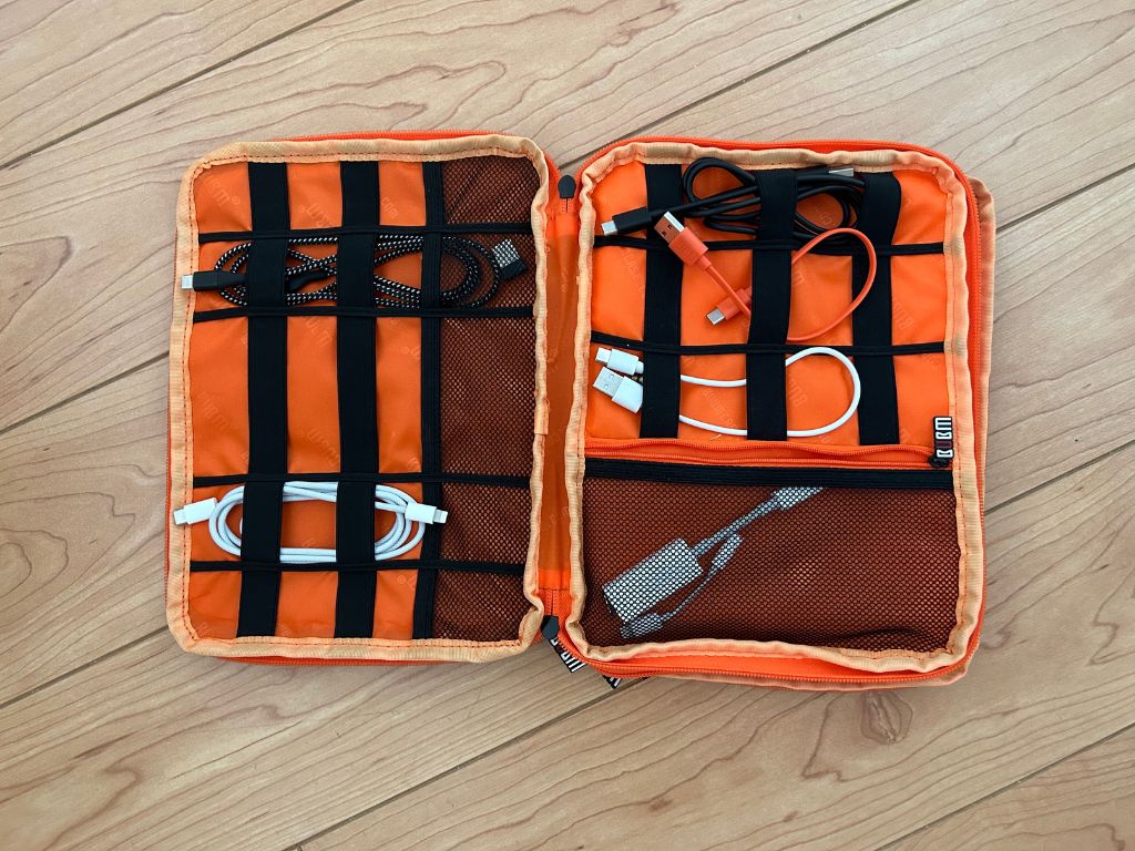An orange travel electronics organizer bag with white and black cords inside